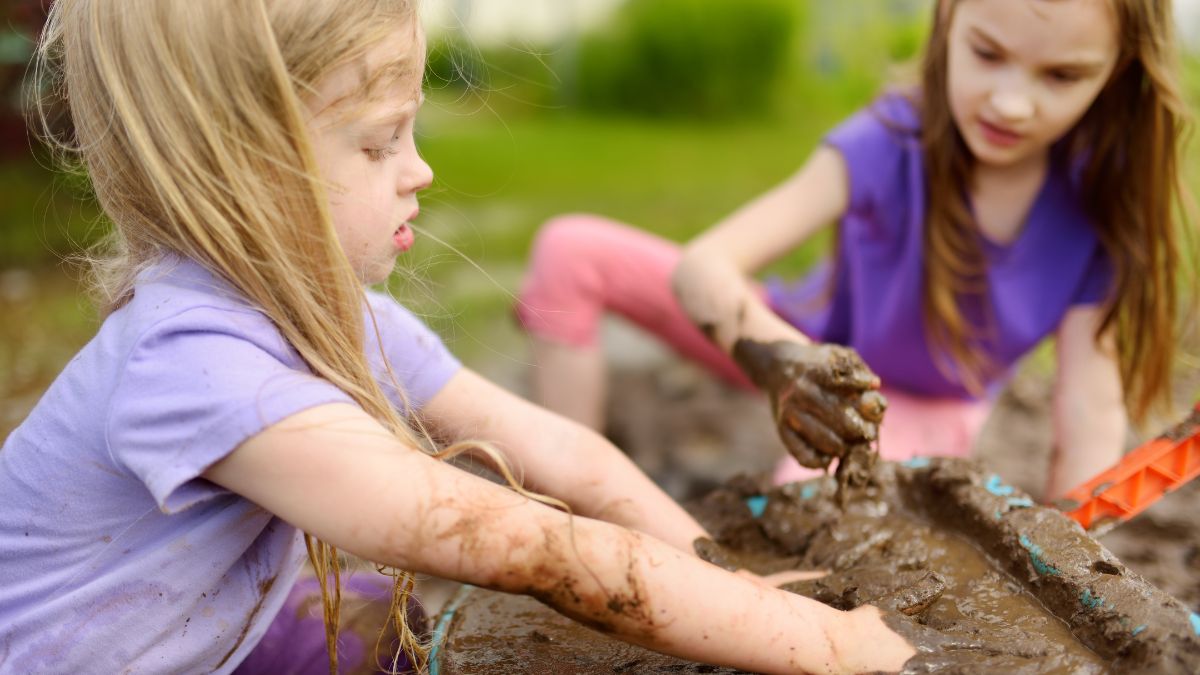 Two young girls play in mud at childcare centre.