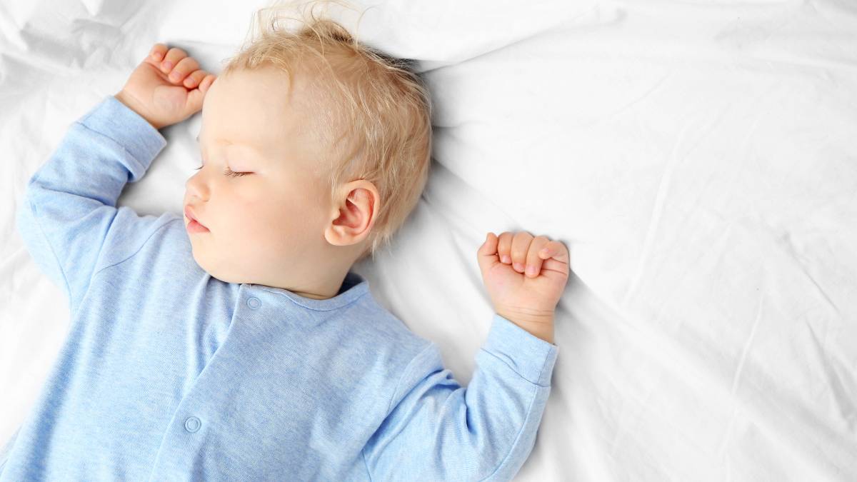 Baby sleeping in cot on back.