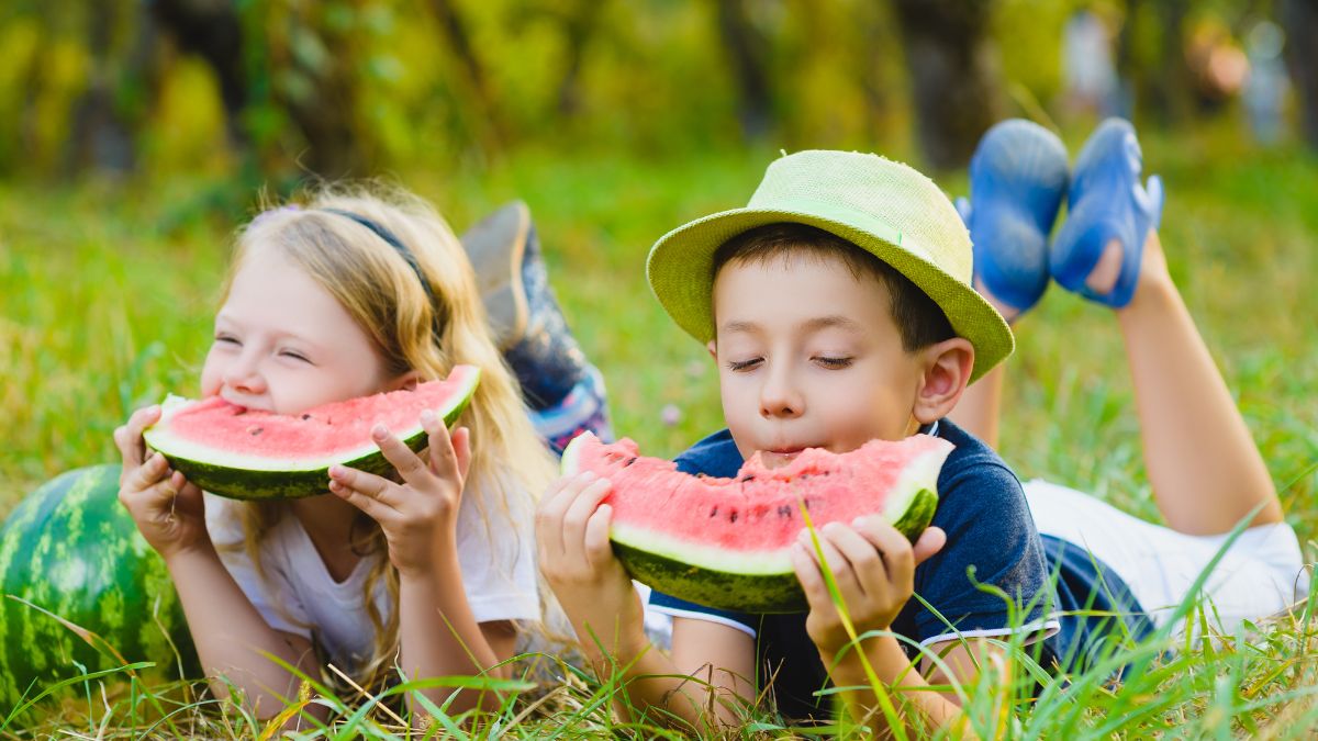 kids sit in grass eating watermelon